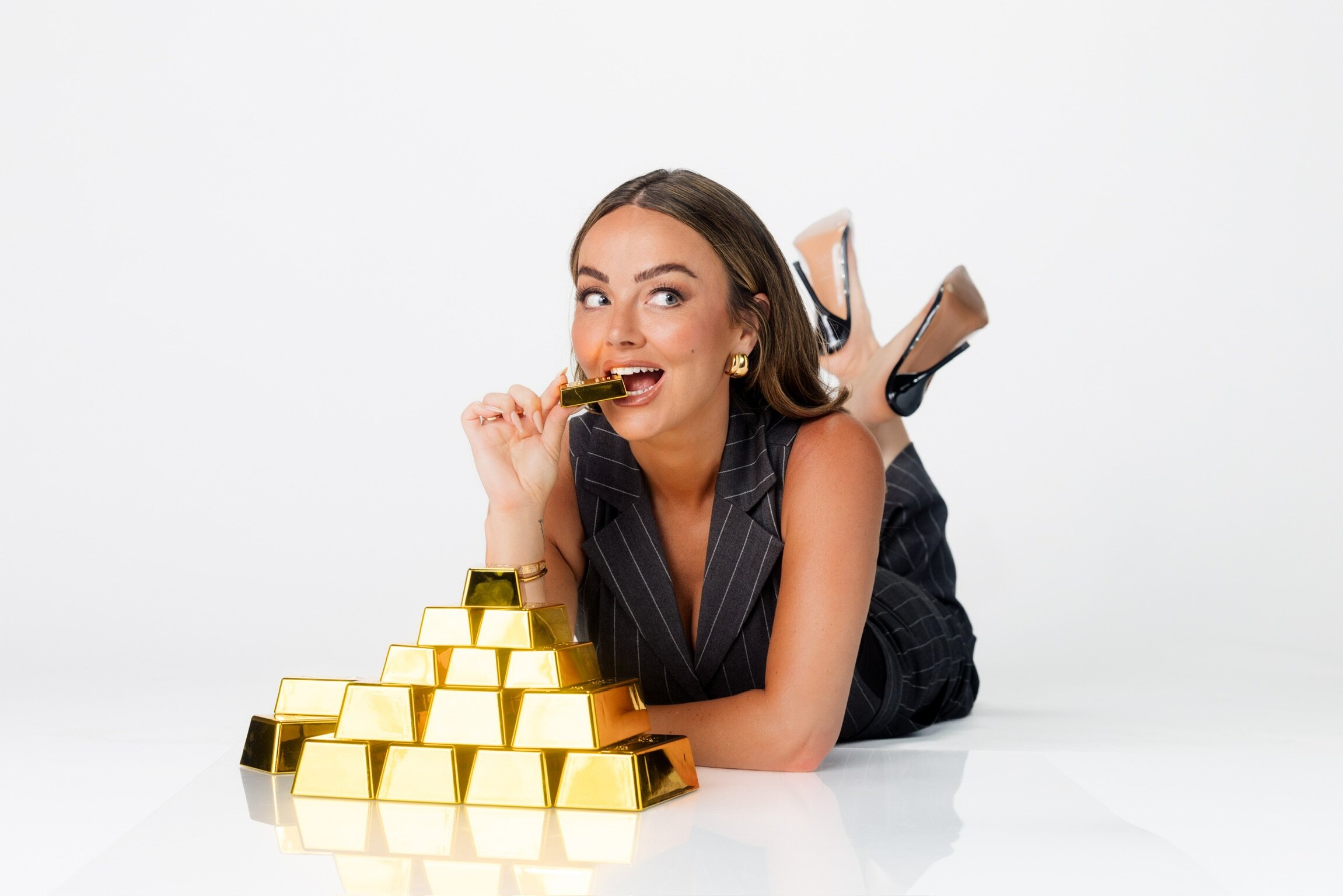 Nicole Lapin playfully biting a gold bar beside a pyramid of gold bars